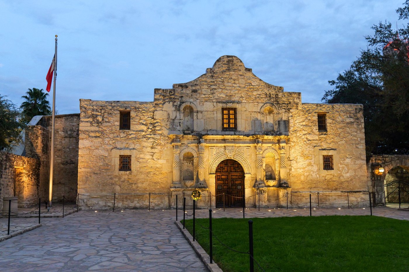 The Alamo in San Antonio, its limestone facade illuminated beneath a blue evening sky